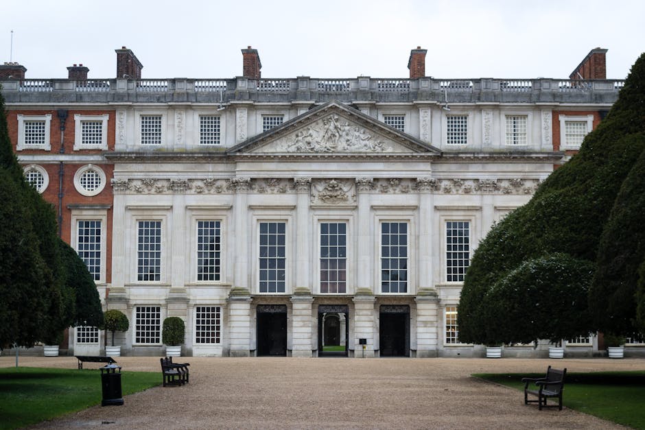 A historic multi-storey building with a symmetrical facade featuring large white-framed sash windows and classical architectural details, including decorative reliefs and a pediment above the central